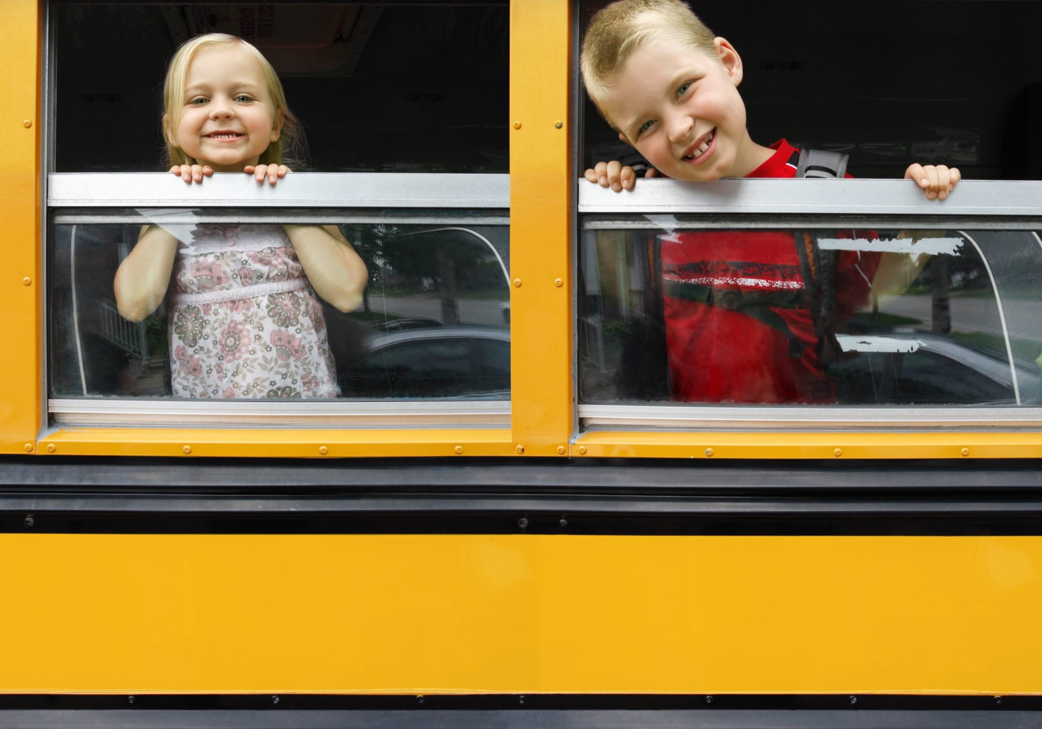 Photo of two happy children looking out the windows of a yellow school bus. Plenty of space for text.